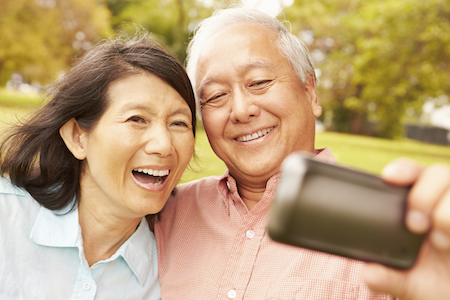 Older Asian couple takes a selfie knowing their smiles look perfect due to dentures from McQueen Dental in Fayetteville, AR.