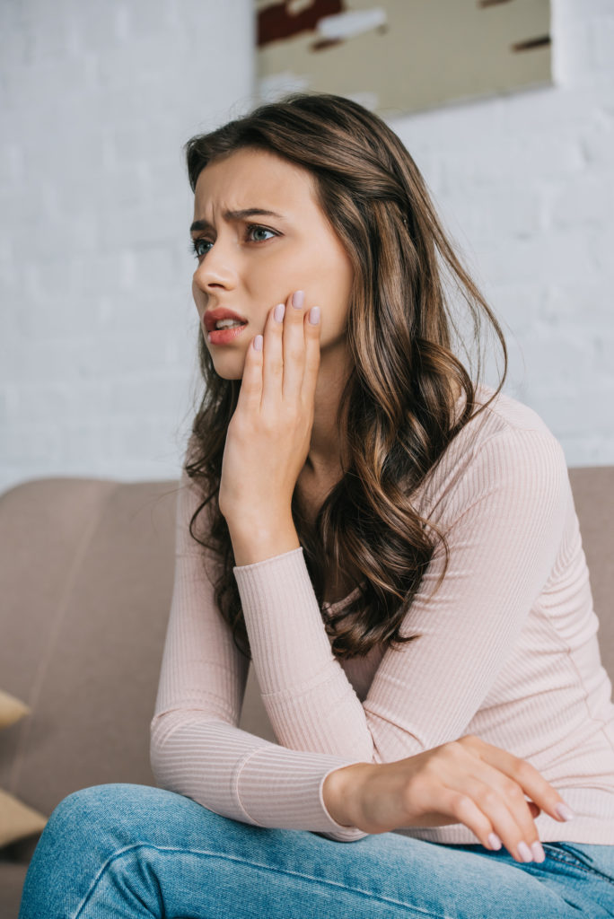 Image of young woman holding the side of her face with pain can be a sign of gum disease.